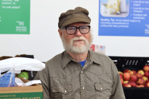 Neighbor at The Share Center Food and Resource Center smiles in front of produce.